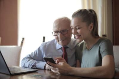 Stock photo of a senior male smiling and looking at a cell phone held by a younger female.