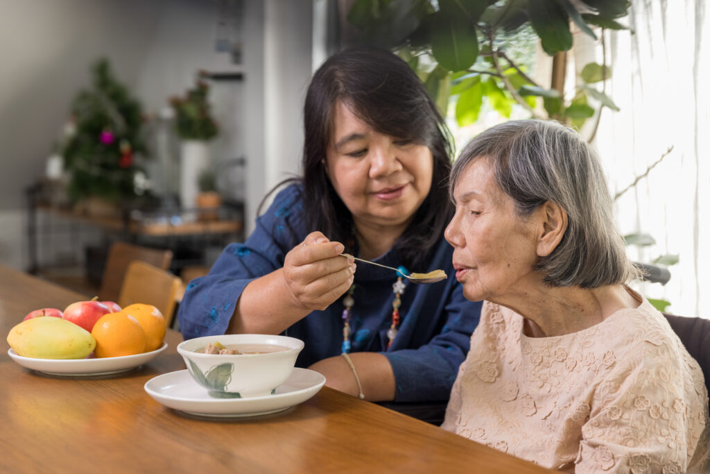 family caregiver serving meal to senior woman