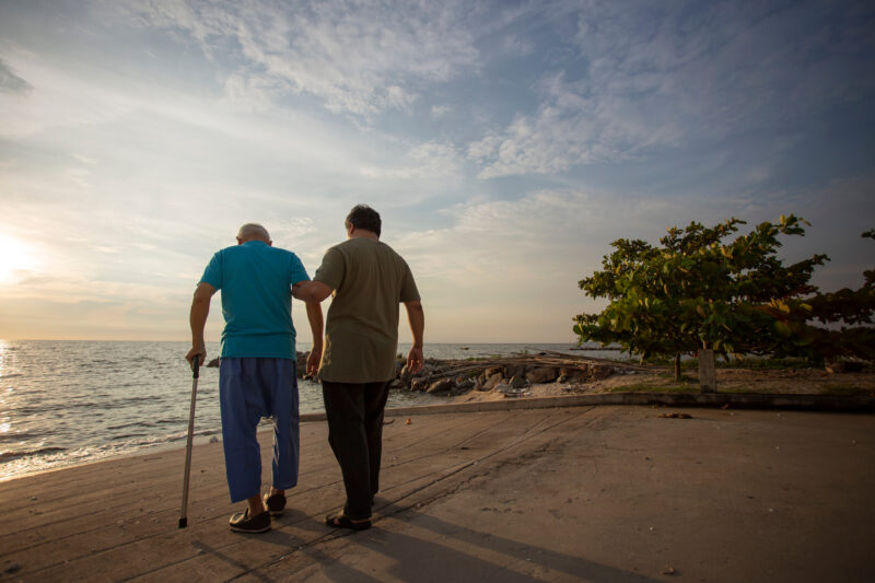 garegiver and senior walking on beach