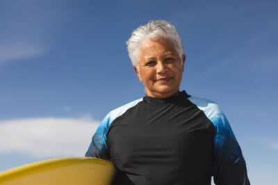woman standing with surfboard in front of blue sky
