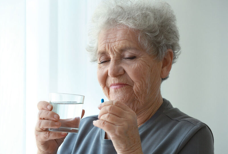 older woman holding a pill supplement and glass of water