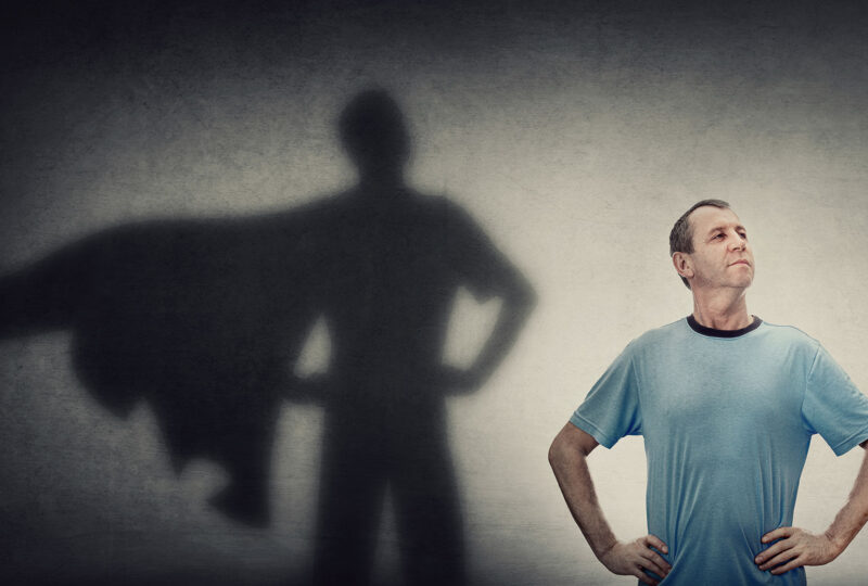man standing in front of wall with shadow with cape behind him