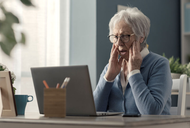 older woman sitting in front of laptop looking shocked