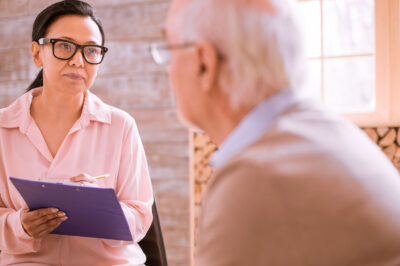 woman with glasses and clipboard talking to older man
