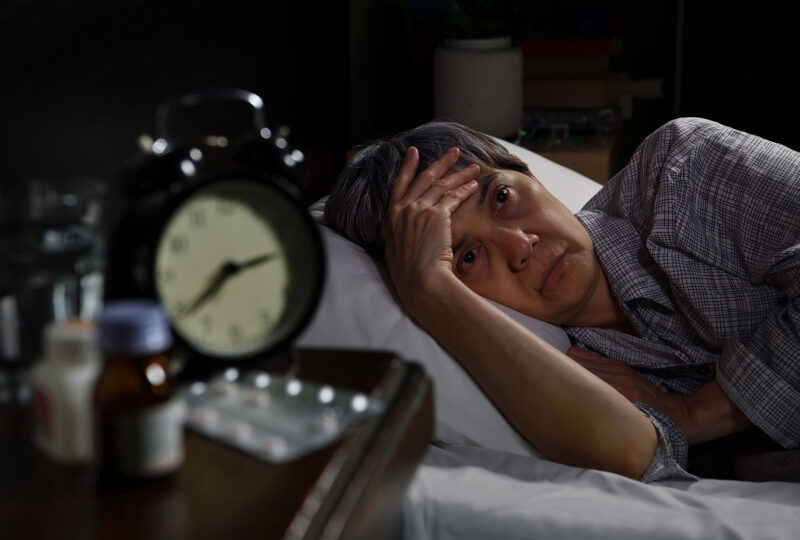 older person in bed awake at night with alarm clock