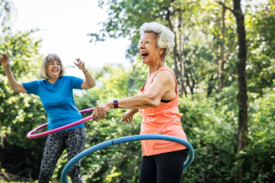 senior older woman hula hooping outside with another woman