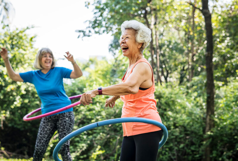senior older woman hula hooping outside with another woman