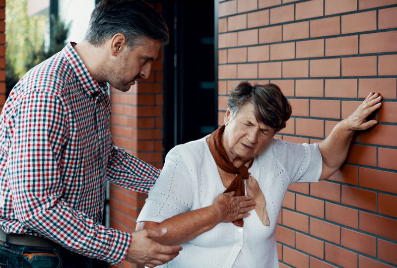 young man aiding older senior woman having shortness of breath leaning against wall