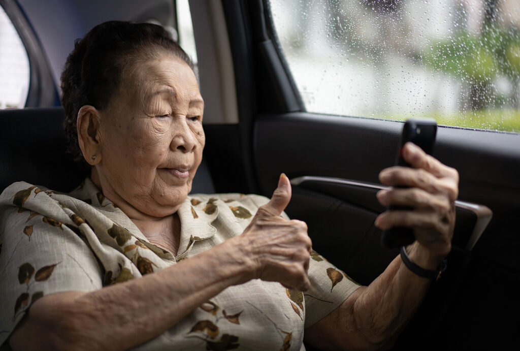 senior woman in back of car with thumbs up to phone