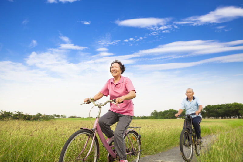 older senior man and woman riding bicycles through a field