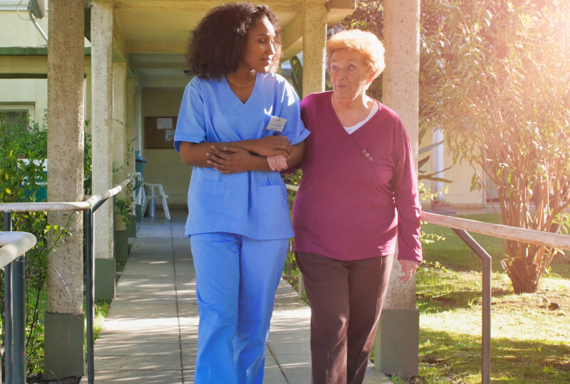 nurse walking outside with older woman at assisted living facility