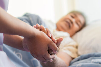 person holding hands of older woman in bed