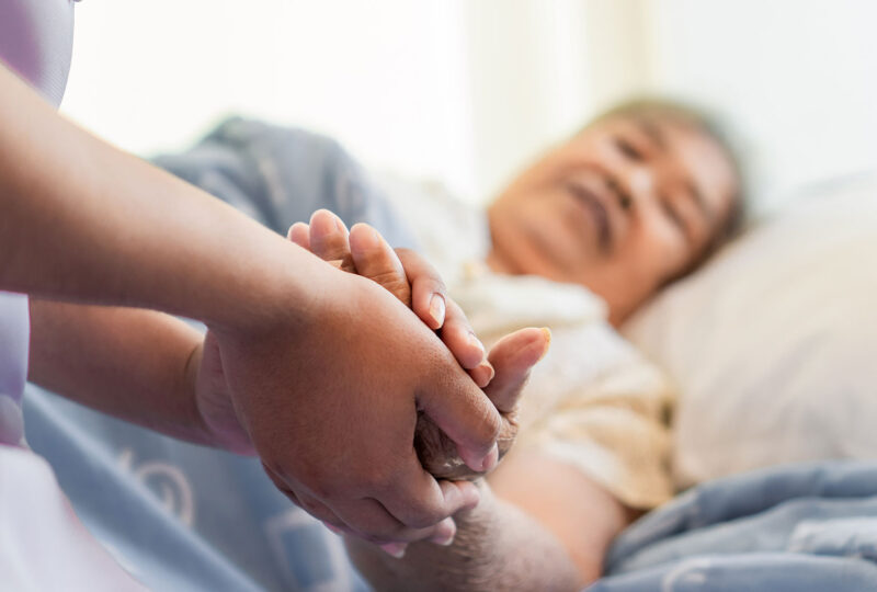 person holding hands of older woman in bed