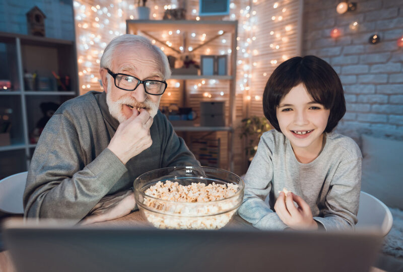older man with boy watching movie and eating popcorn