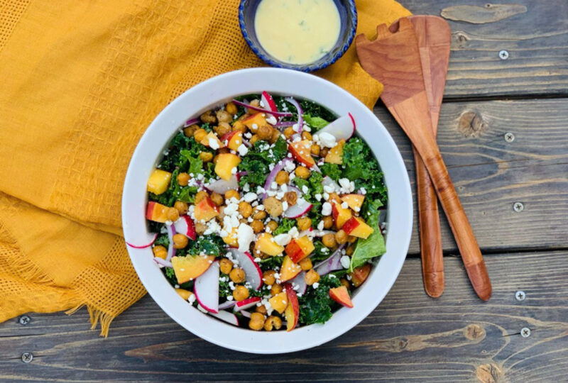 kale and chickpea salad in a bowl next to sauce and mixing spoons on a table