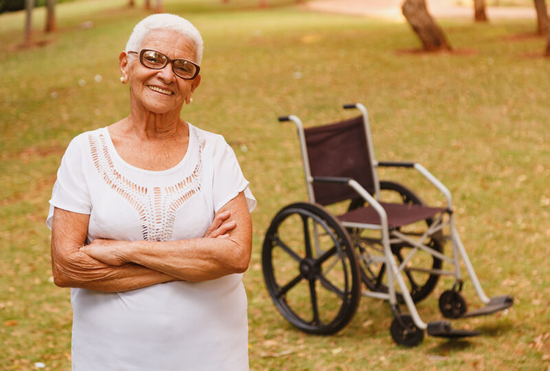 senior person standing outside with arms crossed in front of wheelchair