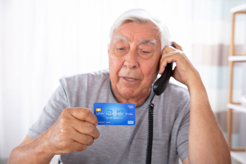 senior man on phone holding up credit card