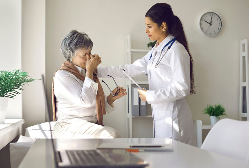 senior woman rubbing eyes, doctor hand on shoulder