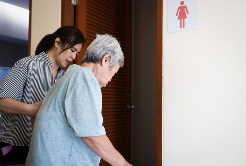 woman helping older woman with walker to the bathroom