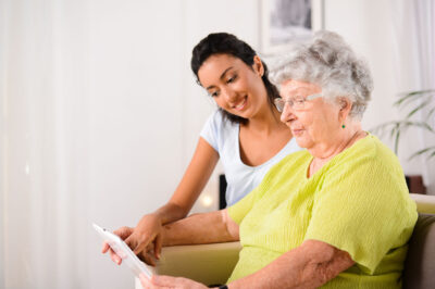 older woman holding tablet, younger woman pointing at it