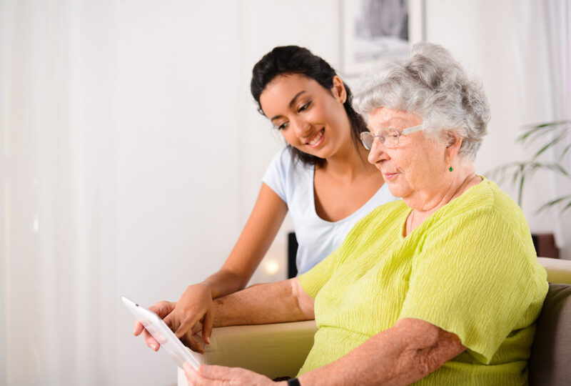 older woman holding tablet, younger woman pointing at it