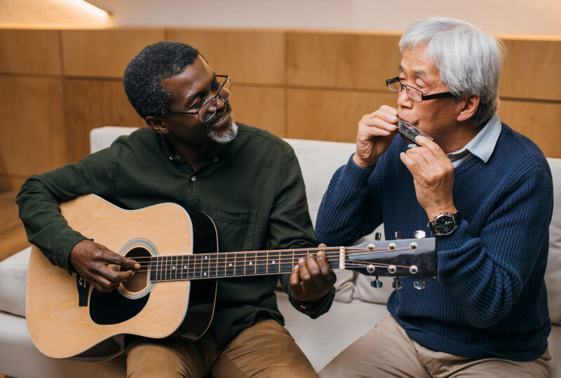 a man playing a guitar sitting next to and looking at a man playing harmonica