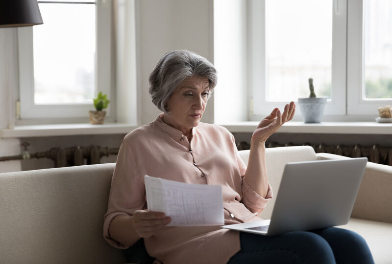 older woman looking at laptop and paperwork confused