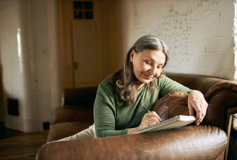 woman sitting on couch writing in a notebook