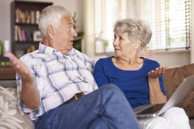 senior couple sitting next to each other on couch with hands up