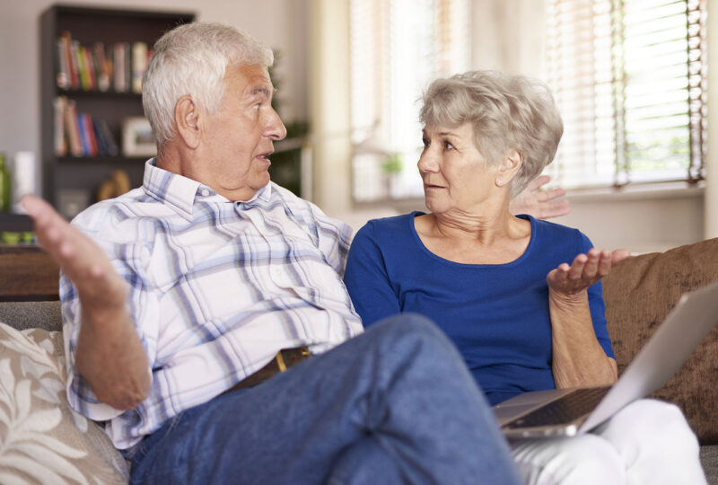 senior couple sitting next to each other on couch with hands up
