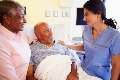 woman standing next to man in hospital bed, smiling at nurse