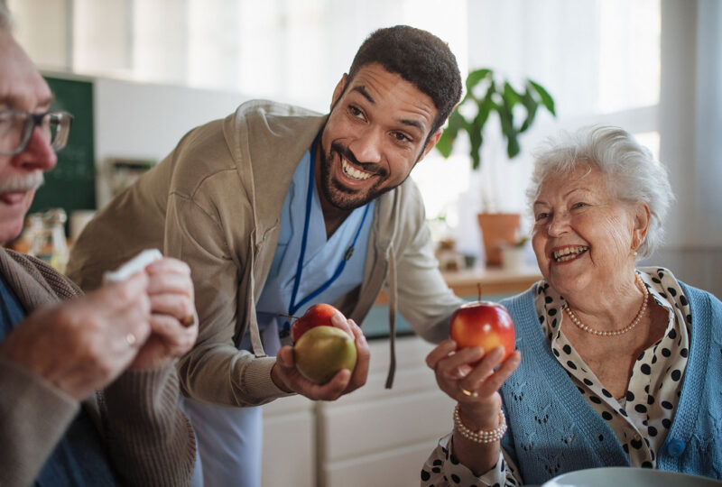 nurse holding up apples to senior man and woman