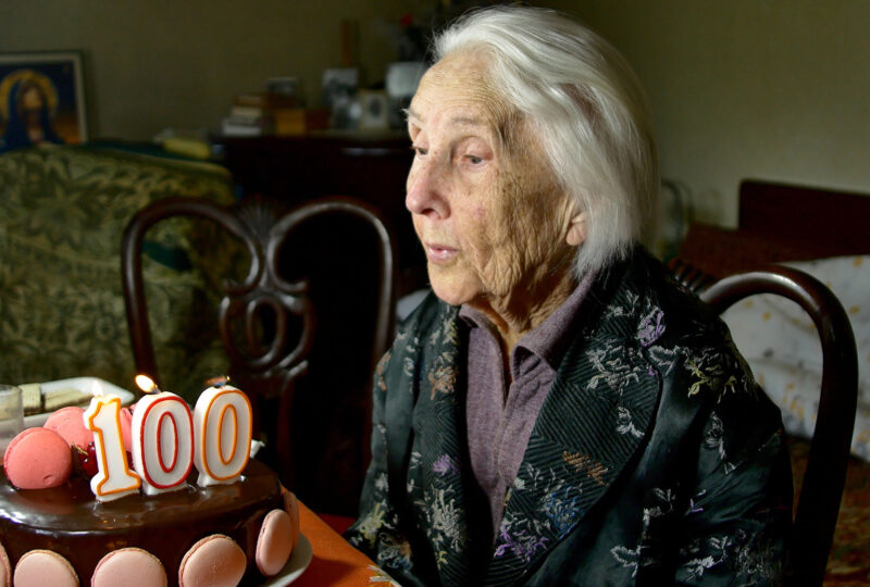 woman blowing out candles on 100th birthday cake