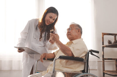 nurse or doctor checking medication being held up by an older man in a wheelchair