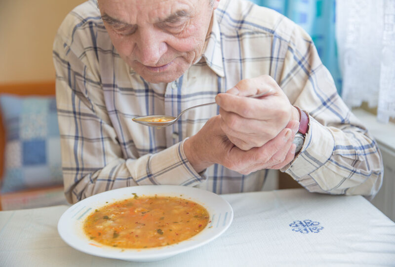 senior man eating soup holding spoon with both hands