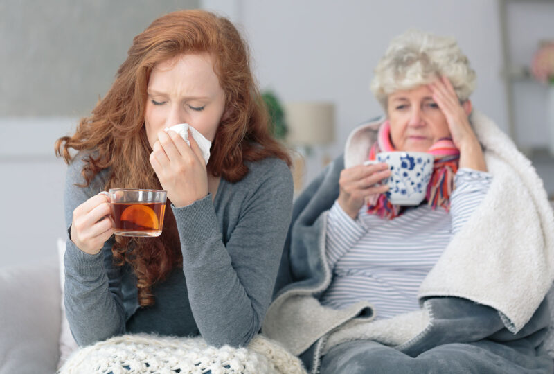older and younger women sitting bundled up with mugs, sick