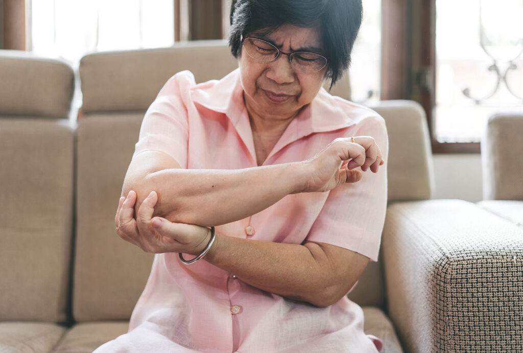 older seated woman clutching her elbow in pain