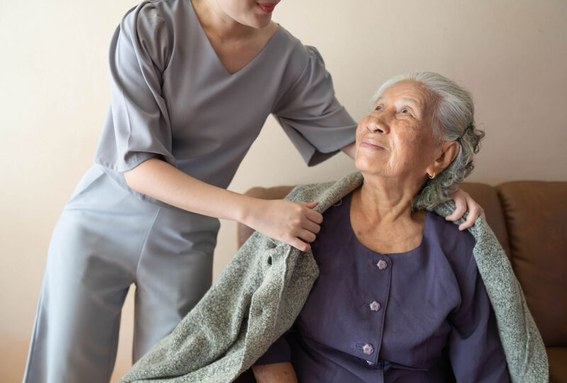 Caregiver covering senior woman with sweater at home