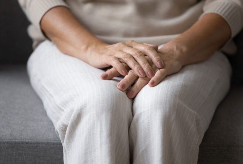 close up of older woman sitting on sofa, holding folded hands on lap