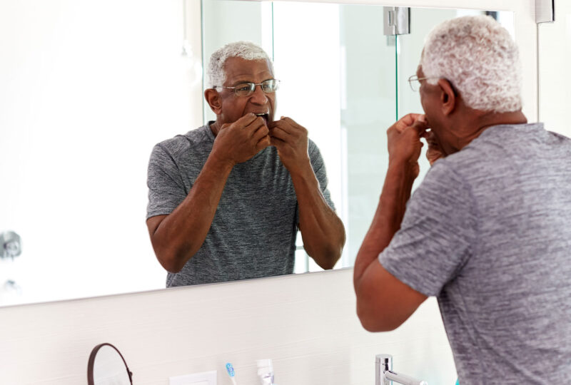 man flossing teeth looking at reflection in bathroom mirror