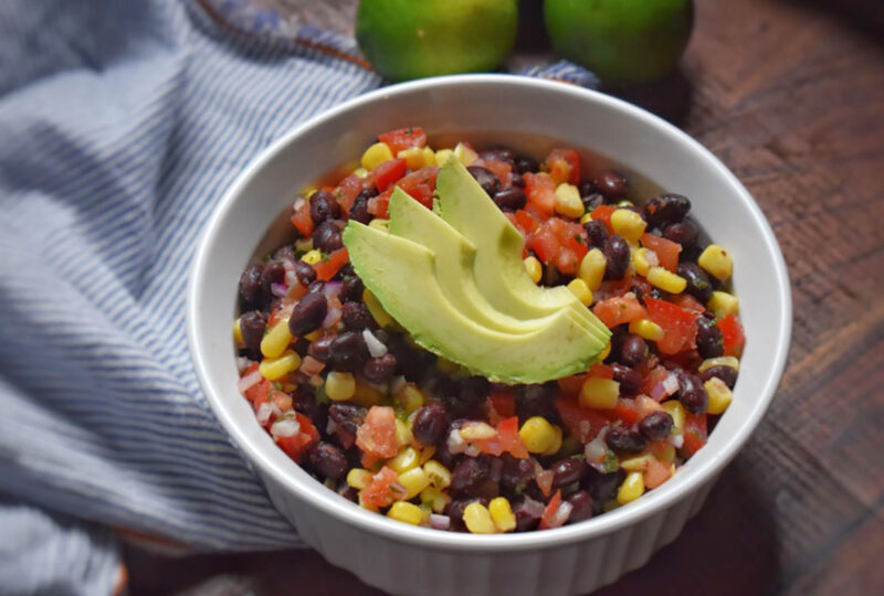 corn and bean salad in a bowl with slices of avocado on top