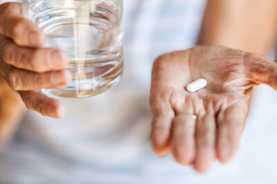 senior woman holding a pill in one hand and a glass of water in the other hand