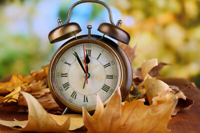 Old clock on autumn leaves on wooden table on natural background
