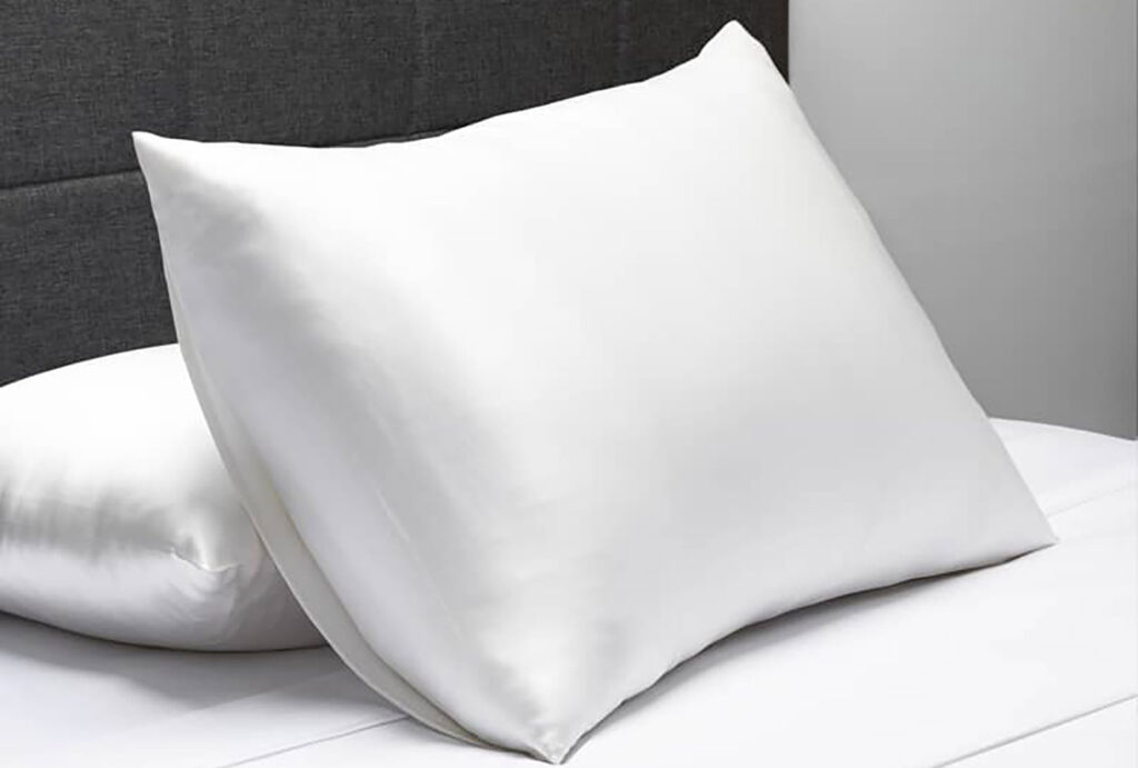 pillow with white silk pillowcase on a bed, leaning against another pillow