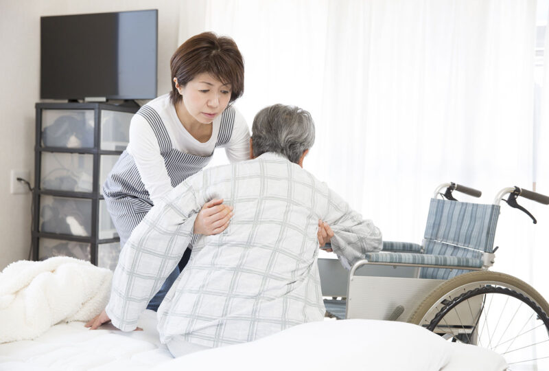 woman helping older person out of bed