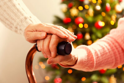 hand resting on a hand on a cane in front of a Christmas tree