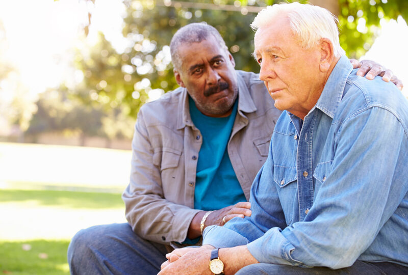 man comforting older friend outside on a bench