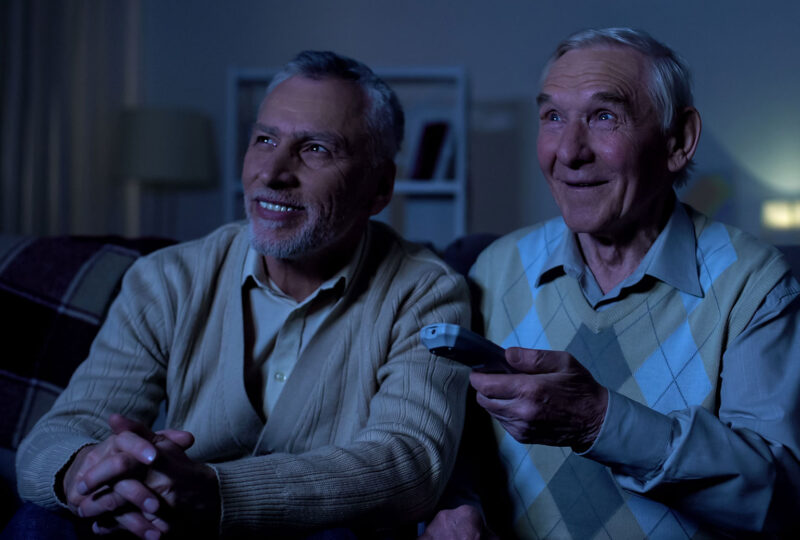 two older men sitting on couch watching tv late at night
