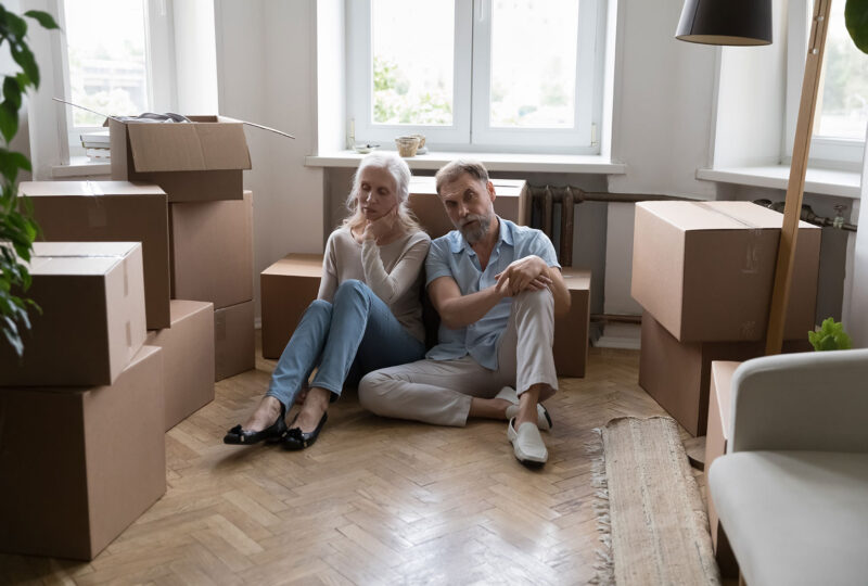 man and woman sitting on floor among boxes, looking tired