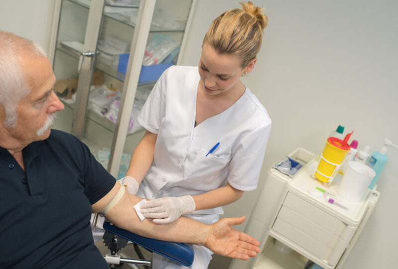 nurse taking blood sample of senior man